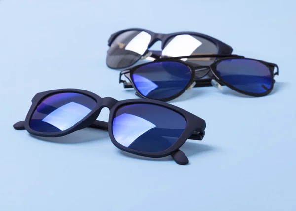 Různé stylové sluneční brýle na modrém tvůrčím pozadí — Stock fotografie