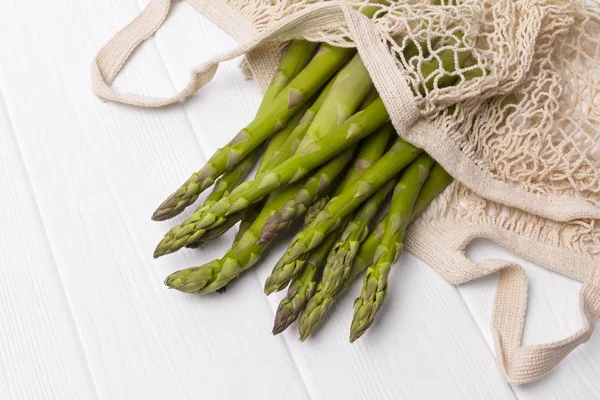 Beyaz ahşap sekme üzerinde dize alışveriş çantası taze yeşil kuşkonmaz