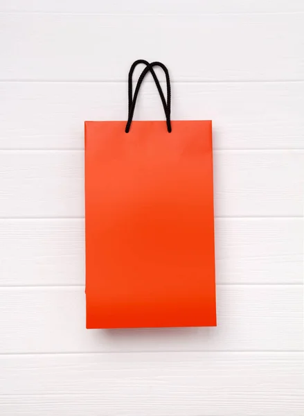 Nákupní taška z oranžového papíru s černými úchyty na bílém dřevěném — Stock fotografie
