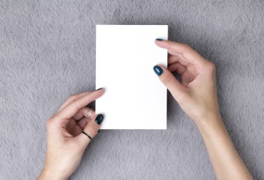 Manicured woman's hands holding postcard on grey furry backgroun