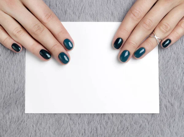 Manicured woman's hands holding postcard on grey furry backgroun — Stockfoto