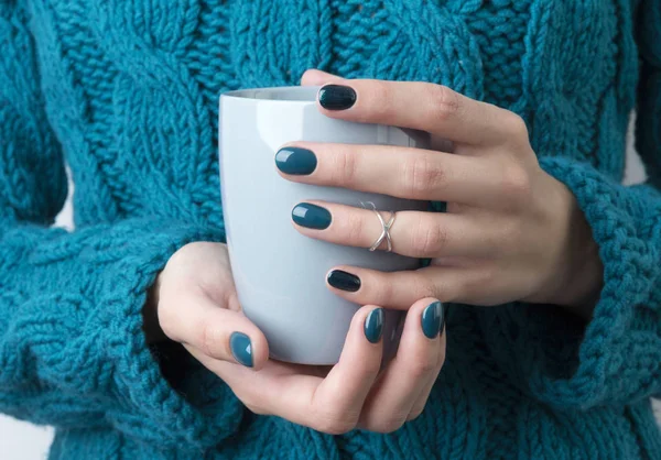 Woman's hands with turquoise manicure hold a grey cup of coffe o — Stockfoto