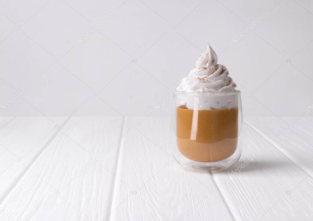 Cocktail with whipped cream on top on white wooden background with copy space.