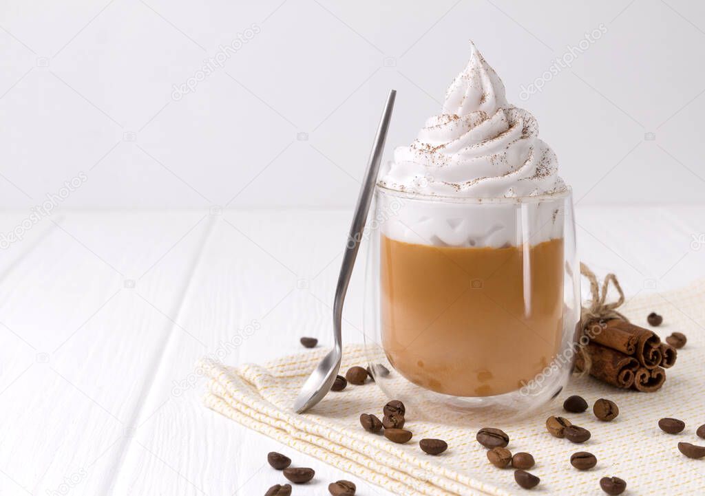 Pumpkin latte with whipped cream and spices on white wooden background