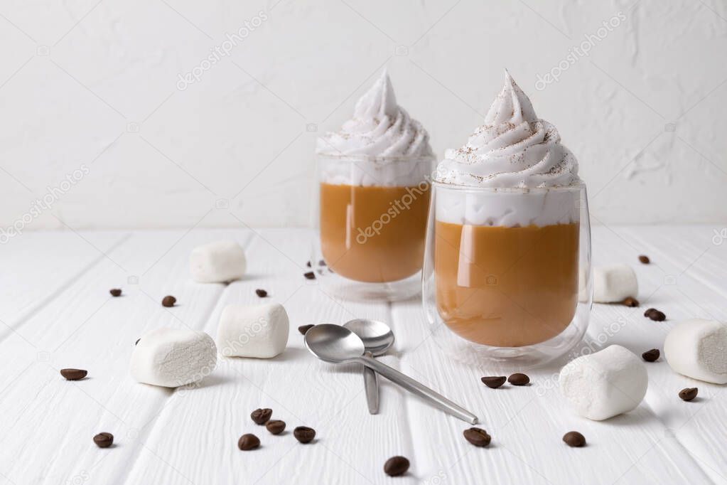 Pumpkin latte with whipped cream and spices on white wooden background.