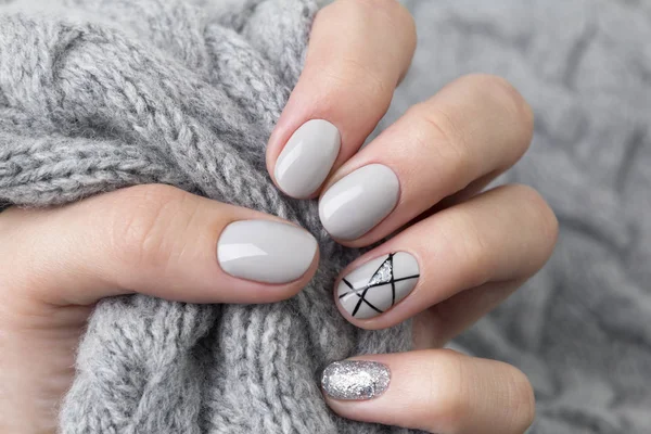 Modern manikürlü kadın eli, gri örülmüş süveteri yakından tutar.