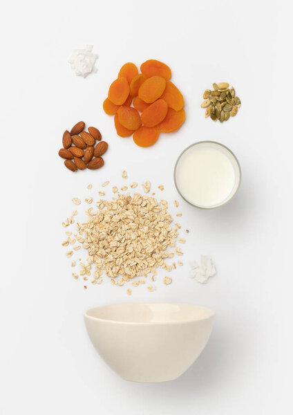 Сушеные абрикосы, миндаль, овсяные хлопья и молоко в керамической миске
