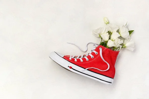 Kreatív kompozíció piros tornacipővel és virágokkal fehér alapon — Stock Fotó