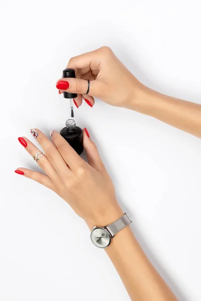 Mano de mujer con manicura roja sosteniendo una botella de esmalte de uñas —  Fotos de Stock