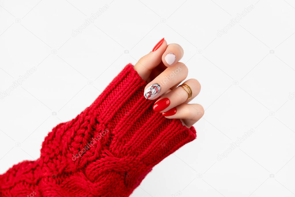Womans hand in sweater with red manicure on gray background