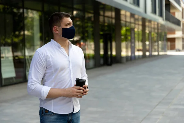 Businessman near office in protective cloth face mask. Man in casual clothes standing on the street. New social behavior new normal concept