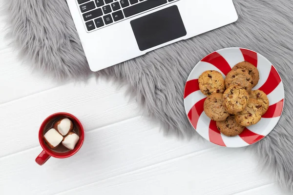 Laptop with cocoa and cookies on furry background. Christmas online shopping working from home concept.