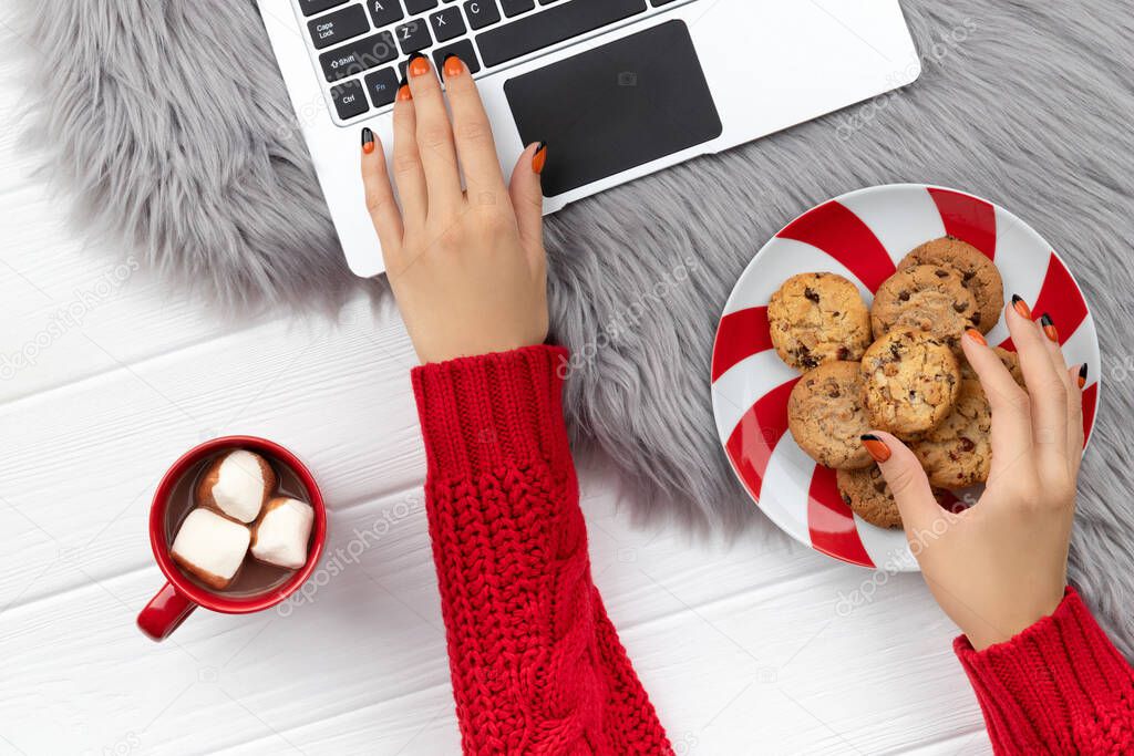 Womans hands typing on the keyboard with cocoa and cookies on furry background. Christmas online shopping working from home concept.