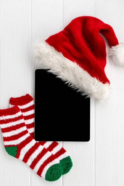 Tableta digital con sombrero de Santa y calcetines sobre fondo de madera blanca — Foto de Stock