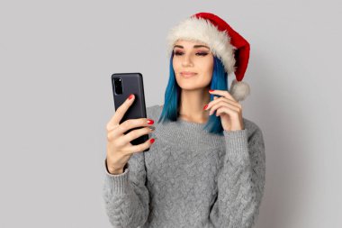 Noel Baba şapkalı güzel mutlu genç kadın gri arka planda selfie çekiyor. Noel yeni yıl kutlaması konsepti