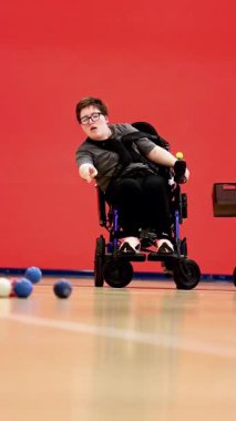 A young athlete engaging in a game of wheelchair boccia, a precision ball sport designed for individuals with cerebral palsy, demonstrating focus and skill on the court.