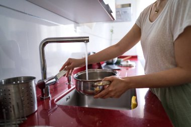 Woman filling a pot with water at the sink in a contemporary kitchen. The setting highlights a casual home lifestyle, focusing on real-life cooking experiences