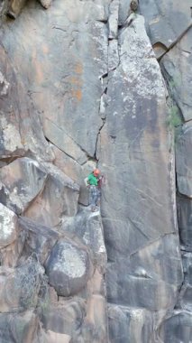 A climber ascends a rugged rock face using traditional climbing gear. The scene highlights gear like hexes and camalots, emphasizing the adventure and skill involved.