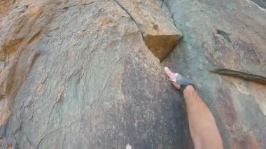 Cropped unrecognizable man climbing a rugged rock face using climbing gear, including ropes and anchors, secured on a rugged rock face. The natural surface displays distinct textures.