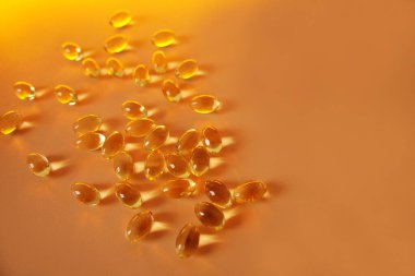 Sayısız balık yağı kapsülü canlı turuncu bir yüzeye yayılarak sağlıklı yaşam için güçlü bir Omega-3 yağ asidi kaynağı sunar.