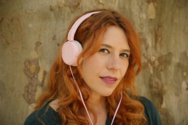 Redhead woman enjoying music with pink headphones in a park