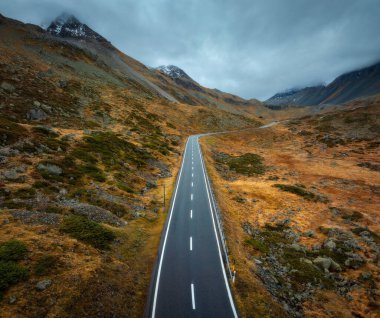 İsviçre 'nin İsviçre Alpleri' ndeki dolambaçlı dağ yolunun hava manzarası. Keskin kıvrımlar, alp dereleri, kayalık yamaçlar, sonbaharda günbatımında dramatik bulutlar. Yolların, sarı çayırların ve tepelerin en yüksek insansız hava aracı manzarası