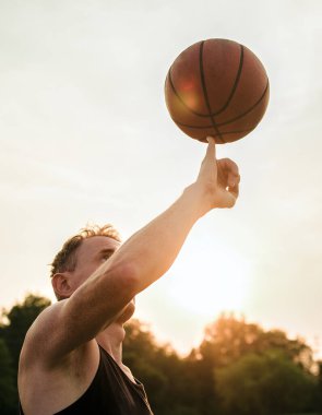 A man balancing a basketball on his pinky finger with natural background and sunset during golden hour in the United States.
