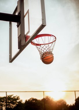 Akşamları potaya düşen bir basket topu ve Amerika 'da arka planda ağaçlar var..