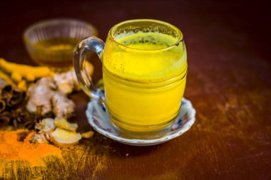 Golden milk with species like green cardamom,turmeric,cinnamon,honey and ginger on wooden surface  clipart
