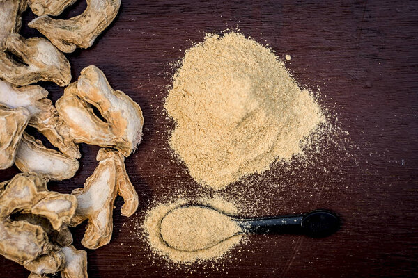 Dried ginger with its powder on wooden surface