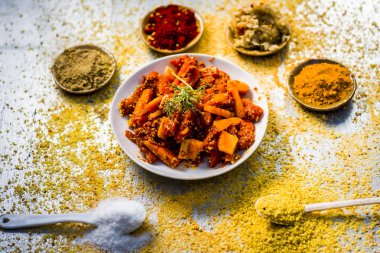 Traditional carrot pickle with  red pepper powder, turmeric powder with ginger garlic paste on wooden background clipart