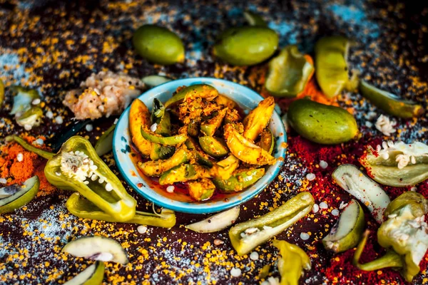 Close up of traditional raw mango pickle with ingredients on table