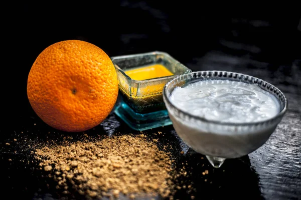 Close up of skin whitening method or remedy i.e. raw orange dried skin powder well mixed with yogurt or curd on wooden surface in a transparent glass cup with raw orange.