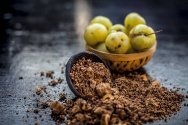 Ham amla veya Phyllanthus emblica veya onun yüz paketi, içecekler ve ahşap yüzeyde doğal ilaçlar kullanılan bir kil kase kuru tohum tozu ile meyve sepeti Hint bektaşi üzümü yakın çekim.