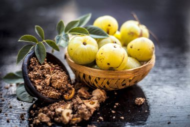 Ham amla veya Phyllanthus emblica veya onun yüz paketi, içecekler ve ahşap yüzeyde doğal ilaçlar kullanılan bir kil kase kuru tohum tozu ile meyve sepeti Hint bektaşi üzümü yakın çekim.;