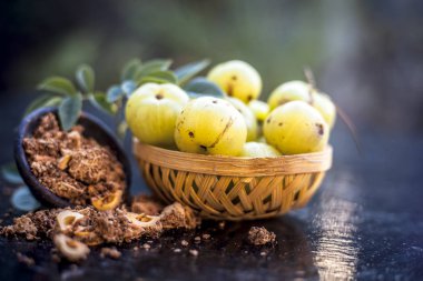 Ham amla veya Phyllanthus emblica veya onun yüz paketi, içecekler ve ahşap yüzeyde doğal ilaçlar kullanılan bir kil kase kuru tohum tozu ile meyve sepeti Hint bektaşi üzümü yakın çekim.;