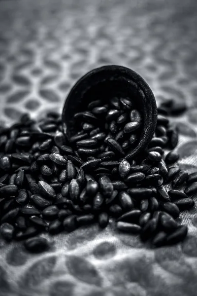 Close up of brown colored dried custard apples or sitaphal or sugar apple seeds in a black colored clay bowl on a brown colored surface. Black and white