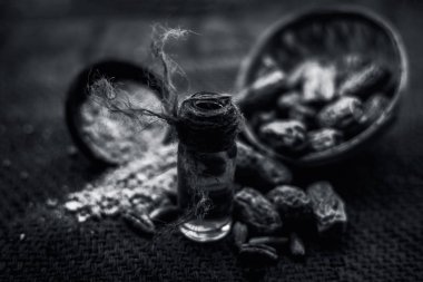 Kurutulmuş hurma veya sukhi khajoor veya Phoenix dactylifera ham kurutulmuş tarihleri ve toz ile kahverengi yüzeyüzerinde şeffaf bir cam şişe içinde kharek Uçucu yağ. Siyah beyaz