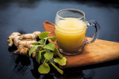 Bazı ham zencefil ve ajwain yaprakları ile ahşap yüzeyüzerinde şeffaf bir cam zencefil organik suyu yakın.