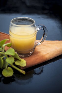 Bazı ham zencefil ve ajwain yaprakları ile ahşap yüzeyüzerinde şeffaf bir cam zencefil organik suyu yakın.