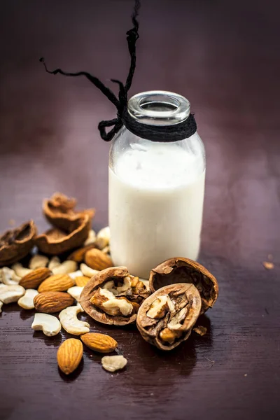 Close up of raw milk in  a glass bottle with walnut in shell  and cracked out on wooden surface.