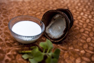 Kahverengi renkli arka plan üzerinde ham hindistan cevizi ile şeffaf bir cam kase hindistan cevizi sütü yakın.