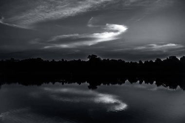 Ağaçlar ve bulutlar ile bir göl üzerinden gün batımı alacakaranlık zaman çekim.
