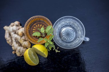 Ahşap yüzeyüzerinde şeffaf bir fincan viski, zencefil, bal, su, limon ve nane oluşan bitkisel yeşil çay yakın.