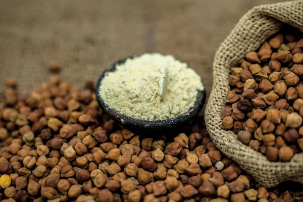 Close up of a jut bag full of chickpeas or grams in it and its floor or besan ka atta in a clay bowl on brown colored surface.