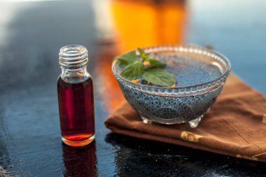 Cam kase ahşap yüzeyüzerinde şeffaf bir cam şişe içinde çıkarılan özü veya uçucu yağ ile ıslatılmış sabja tohumları veya falooda tohumları veya tatlı fesleğen tohumları dolu.