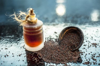 Ham organik bitkisel baharat Hardal tohumu veya sarso veya rai veya Brassica nigra, şeffaf bir cam şişe onun çıkarılan uçucu yağ ile ahşap yüzeyüzerinde bir kil kase içinde.