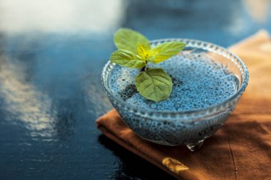 Ilımlı sabja tohumları veya falooda tohumları veya tatlı fesleğen tohumları ahşap yüzeyüzerinde kahverengi renkli peçete üzerinde cam bir kase içinde bazı nane yaprakları ile kapatın. Birçok aromalı içecekte kullanılır.