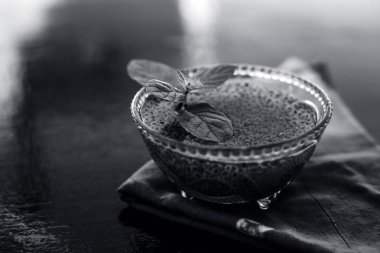 Ilımlı sabja tohumları veya falooda tohumları veya tatlı fesleğen tohumları ahşap yüzeyüzerinde kahverengi renkli peçete üzerinde cam bir kase içinde bazı nane yaprakları ile kapatın. Birçok aromalı içecekte kullanılır.