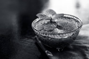 Ilımlı sabja tohumları veya falooda tohumları veya tatlı fesleğen tohumları ahşap yüzeyüzerinde kahverengi renkli peçete üzerinde cam bir kase içinde bazı nane yaprakları ile kapatın. Birçok aromalı içecekte kullanılır.
